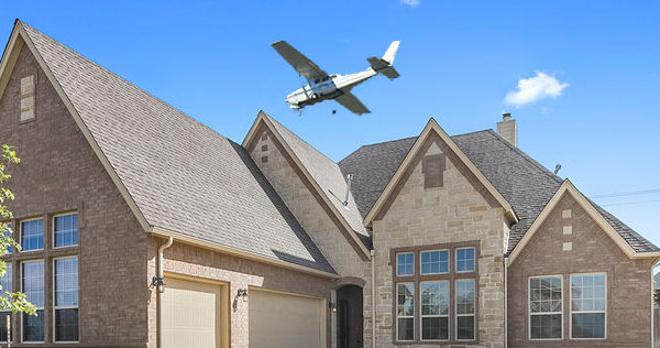 Cessna airplane taking off from airport runway by neighborhood home, creating noise pollution complaints. Flight school operates out of airport, training student pilots on flight.